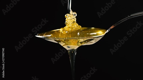 Close up honey flowing from metal spoon on black