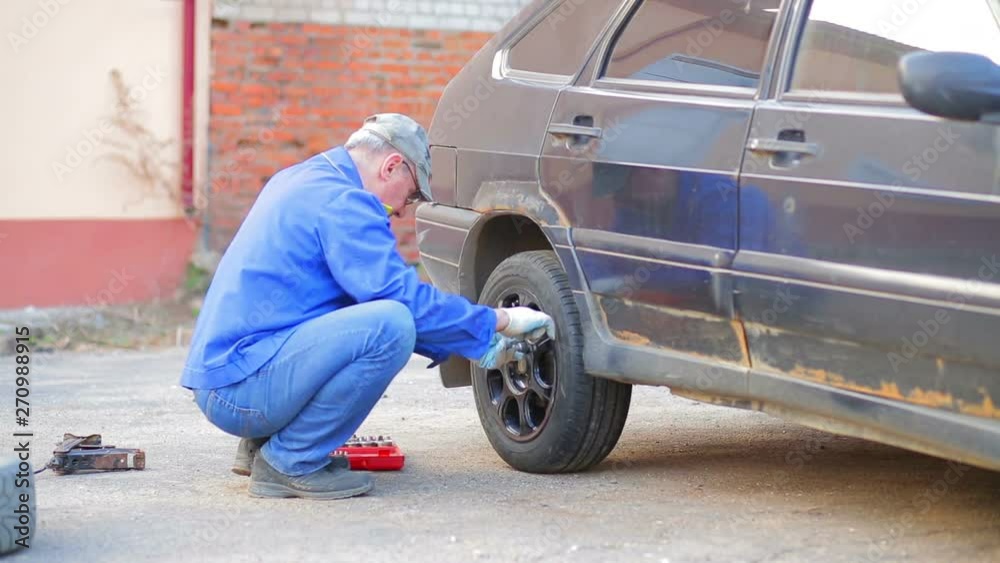 Male auto mechanic with a wrench secures a car wheel Male auto mechanic with a wrench secures a car wheel