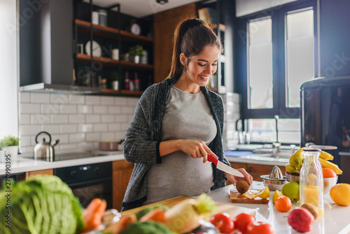 Obraz na plátně Beautiful smiling young pregnant woman preparing healthy food with lots of fruit