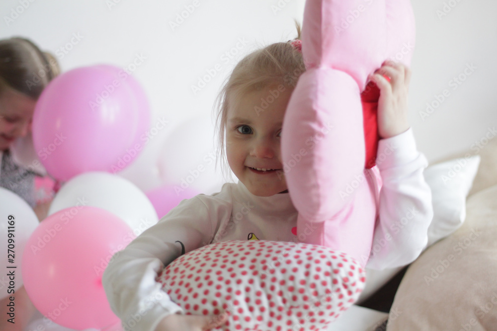 two girls play in bed with white and pink balloons and a strawberry pillow