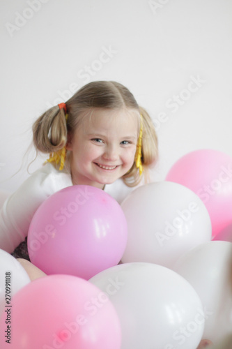 two girls play in bed with white and pink balloons and a strawberry pillow