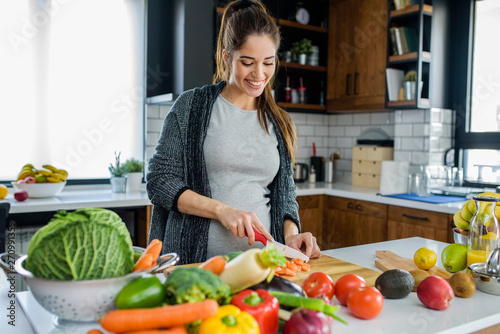 Beautiful smiling young pregnant woman preparing healthy food with lots of fruit and vegetables at home kitchen