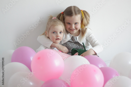 two girls play in bed with white and pink balloons and a strawberry pillow