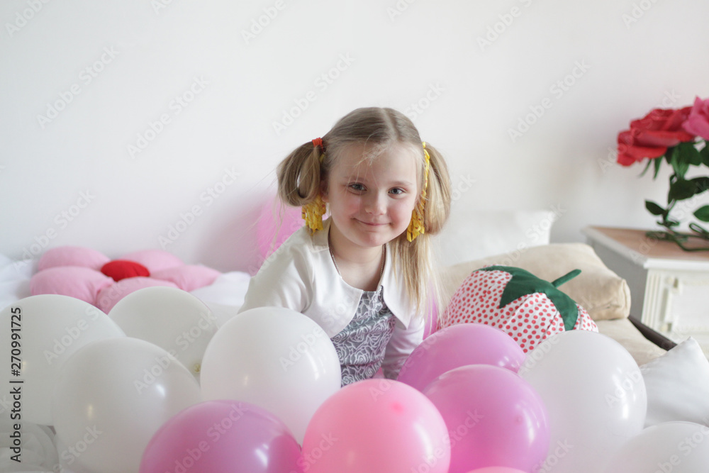 a girl plays in bed with white and pink balloons and a strawberry pillow