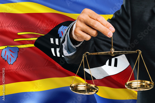 Foto Swazi Judge is holding golden scales of justice with Swaziland waving flag background