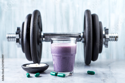 Fototapeta Naklejka Na Ścianę i Meble -  Glass of Protein Shake with milk and blueberries, Beta-alanine and L-Carnitine capsules and a dumbbell in background. Sports bodybuilding nutrition. Stone / Wooden background. Copy space.  