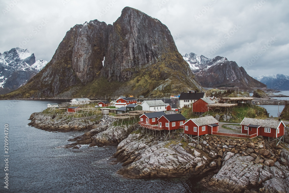 Classic and beautiful landscape of the Lofoten Islands with red fishermen's houses in front of the sea and high mountains in the background, Northern Europe, Norway