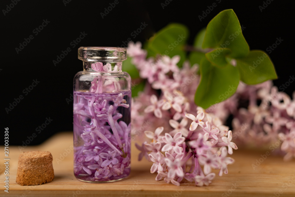 Naklejka Lilac flowers and essential oil in a glass vessel. Ecological preparations on a wooden board.