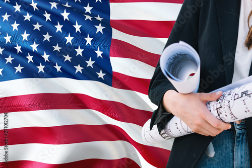 American Architect woman holding blueprint against United States of America waving flag background. Construction and architecture concept. © sezerozger