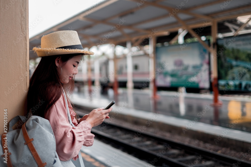 Smiling woman traveler with backpack holding smartphone on holiday relaxation at the train station,relaxation concept, travel concept