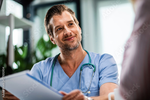 Smiling male doctor talking to his patient while going through medical reports at his office. photo