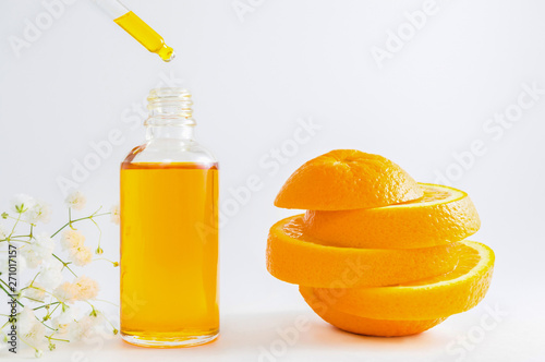 Vitamin C serum in cosmetic bottle with dropper, sliced orange and flowers on white background. Organic SPA cosmetics with herbal ingredients.