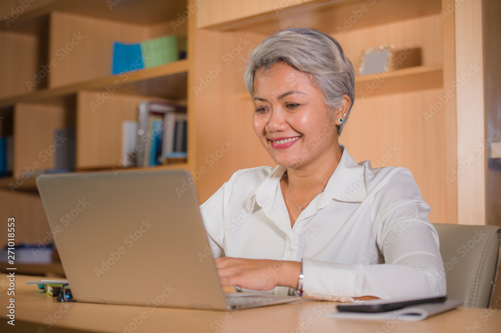 lifestyle office portrait of attractive and happy successful middle aged Asian woman working at laptop computer desk smiling confident in entrepreneur business success lifestyle office portrait of attractive and happy successful middle aged Asian woman working at laptop computer desk smiling confident in entrepreneur business success