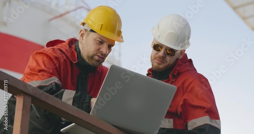 Two male caucasian industrial workers discuss work using laptop photo