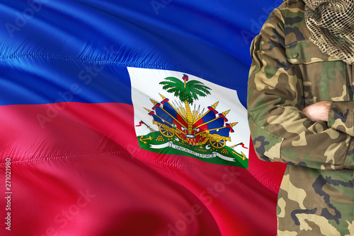 Crossed arms Haitian soldier with national waving flag on background - Haiti Military theme.
