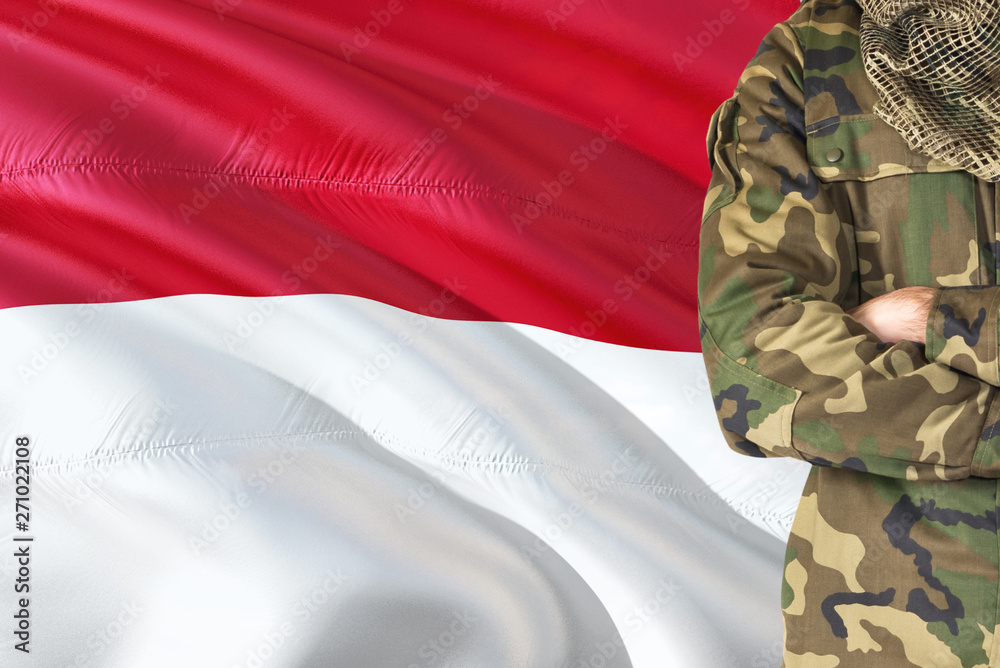 Crossed arms Indonesian soldier with national waving flag on background - Indonesia Military theme. Crossed arms Indonesian soldier with national waving flag on background - Indonesia Military theme.