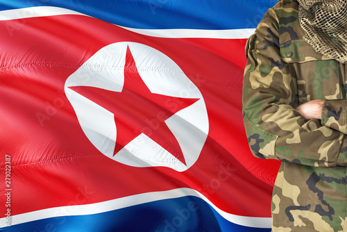 Crossed arms North Korean soldier with national waving flag on background - North Korea Military theme. photo