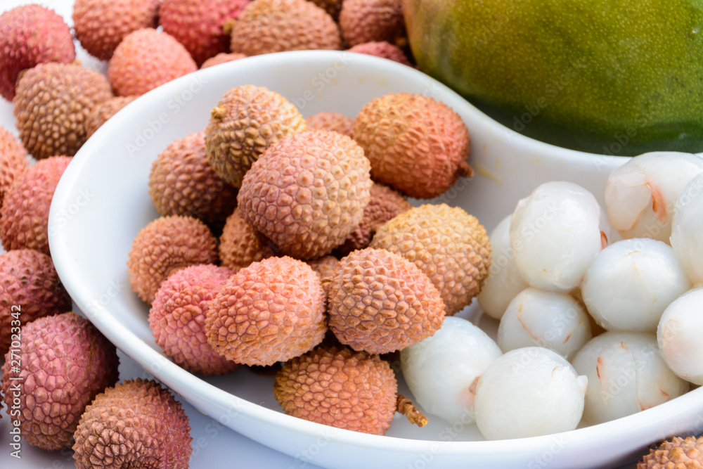 Two ripe mangoes surrounded by ripe litchi fruits on a plate on a white background. Ripe lychee without shell.