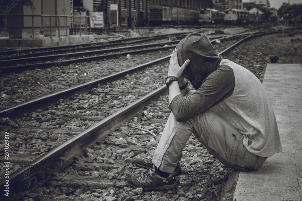 Depressed young man sitting head in hands on the railway platform alone, Sad man, Cry, drama concept, hipster sad.