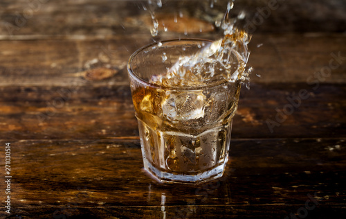 Whiskey splash. Glass of whiskey with ice cubes splashing out.