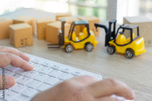 Hand using mouse and keyboard and stack of boxes and mini forklift truck nearby. Consumer can buy product directly anywhere anytime from seller using web browser. Online shopping and ecommerce concept