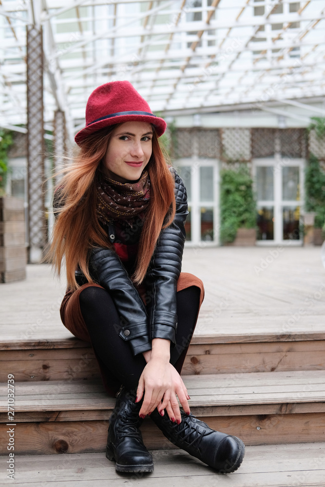 Sensual woman in a red bowler hat with long hair. Smiling girl sitting on wooden stairs. Sensual woman in a red bowler hat with long hair. Smiling girl sitting on wooden stairs.