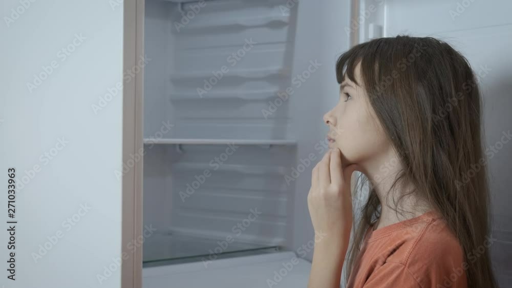 Poverty in childhood. A young girl looks thoughtfully into an empty refrigerator. Poverty in childhood. A young girl looks thoughtfully into an empty refrigerator.