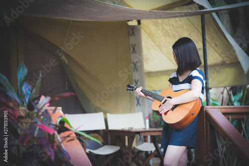 Young cute Asian girl Japanese hipster playing guitar at tent camping campfire party while travelling at beautiful sky mountains scenery views 