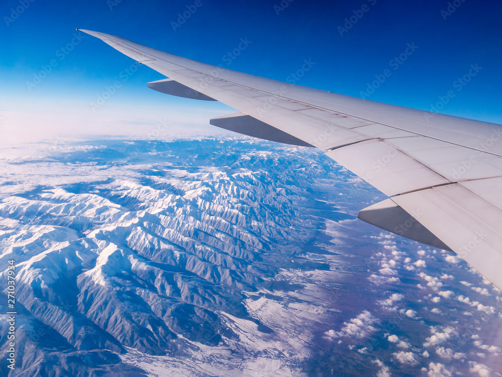 Obraz premium Aerial view of Taurus Mountains covered with snow. Airplane wing while flying seen through window of passenger aircraft. Flying at 35000 feet over ground.