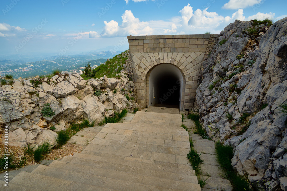 View from the mountain peak Lovchen on a sunny day. Blue sky with clouds, steps leading into the tunnel.