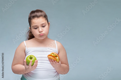 Portrait of a young beautiful girl holding a red Apple in one hand and a hamburger in the other on a white background .A true expression of positive emotions. the problem of childhood obesity
