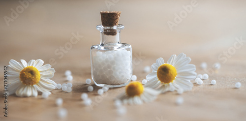 Fotografie Miniatur Glasfläschchen mit Globuli und Kamillenblüten