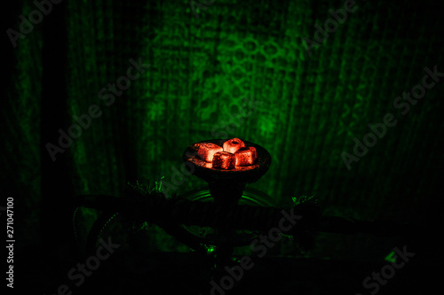 Hookah hot coals on shisha bowl on dark foggy background. Stylish oriental shisha.