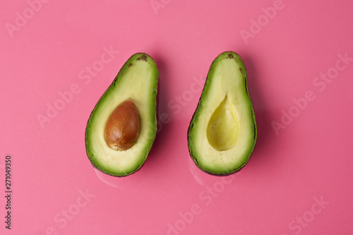 Two halves of avocado haas on a pink background