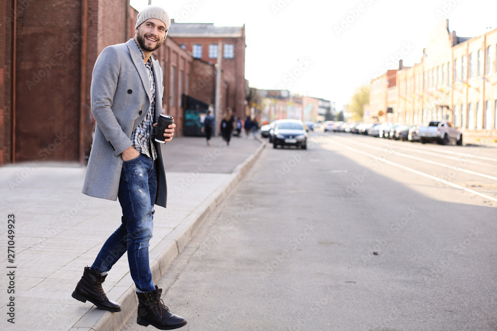 Handsome young man in grey coat and hat crossing the street with a cup of coffee. Handsome young man in grey coat and hat crossing the street with a cup of coffee.