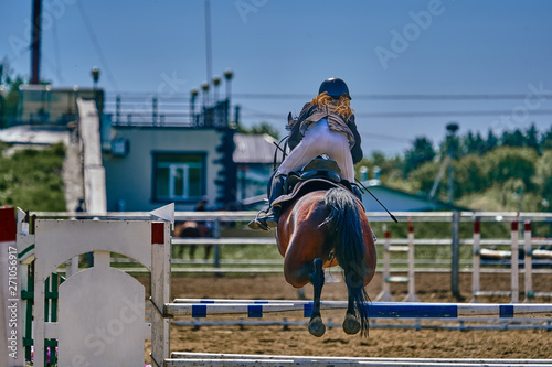 A young woman jockey on a horse performs a jump across the barrier. Competitions in equestrian sport. Close-up.