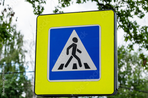 Road sign pedestrian crossing on a blurred background of green trees.