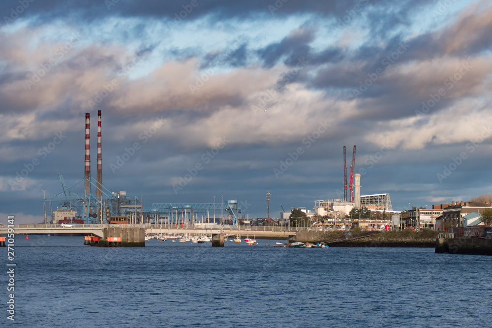 Wide view over docks area in Dublin, Ireland with many boats, cranes and Poolsbeg Power Station chimneys