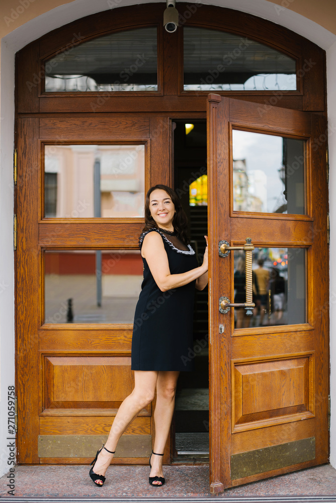 Brunette woman peeking out of beautiful wooden doors and smiling