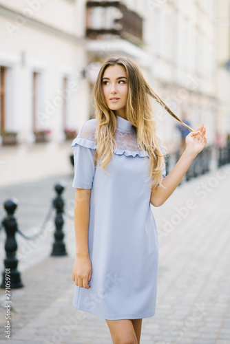 Beautiful young girl in a blue dress holds in her hands a strand of their hair and looks into the distance