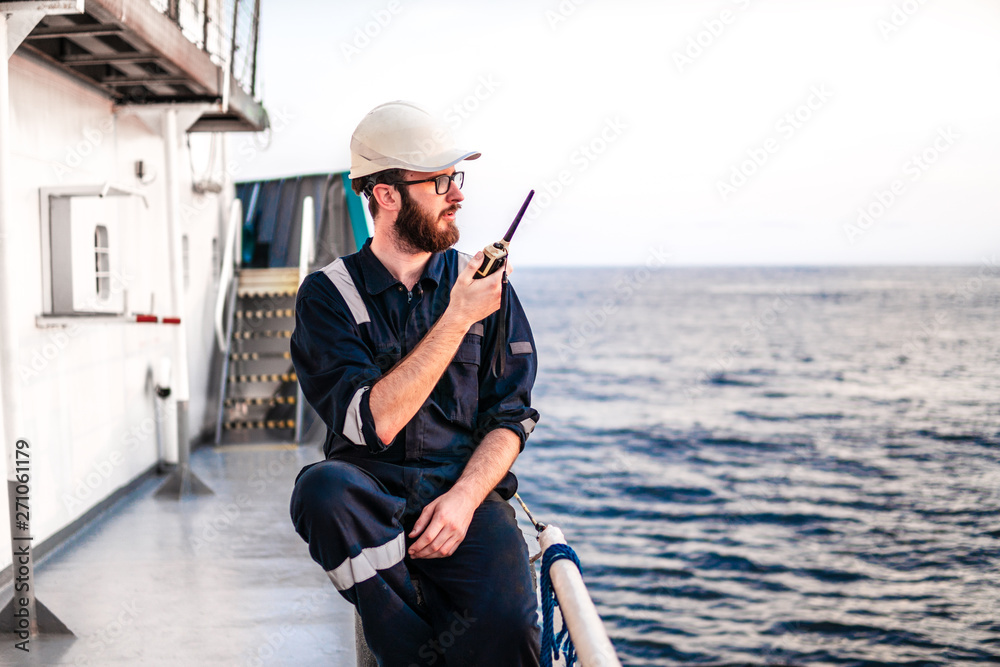Obraz premium Deck Officer on deck of offshore vessel or ship , wearing PPE personal protective equipment. He holds VHF walkie-talkie radio in hands. Dream work at sea