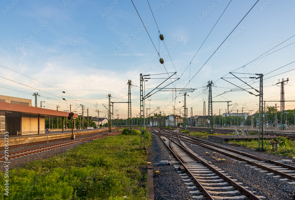 Outdoor view of straight and curve railway track lines without train at train station with mess complex electric cables and poles with golden light atmosphere against evening before sunset sky.