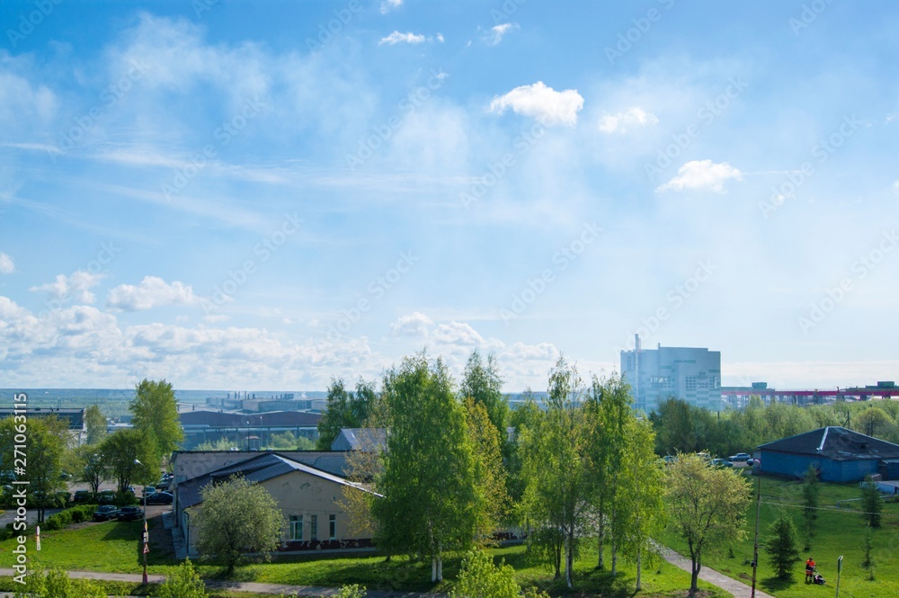 Fototapeta premium Summer industrial landscape - the roofs of industrial buildings against the blue sky with white clouds, in the background - thermal power plants and overhead crane