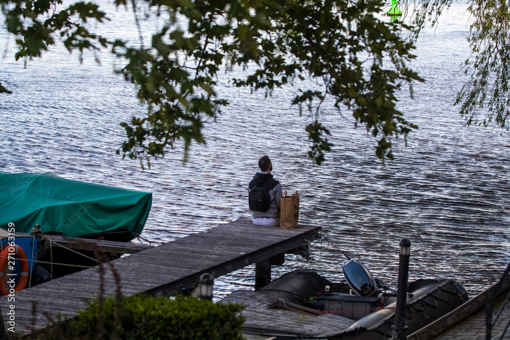 The young and stylish guy with a beard walks near the river and boats. Thoughtful mood. Looks at water. The young and stylish guy with a beard walks near the river and boats. Thoughtful mood. Looks at water.