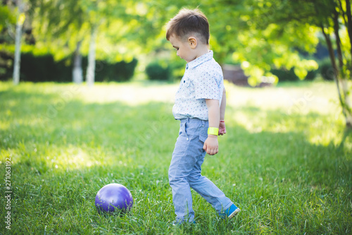 Sporty cute positive kid, playing happily with big ball on green meadow.little boy play in green grass © Delete