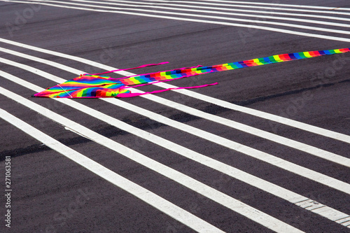 A colorful kite lying on the ground with stripped white lines. Tone image.