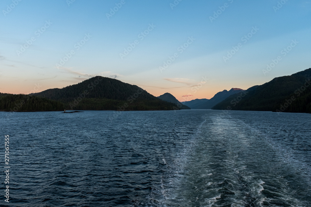 The view at sunset from the back of a ferry as it makes its way through the Inside Passage off the rugged west coast of Canada, the light fading in the distance, nobody in the image
