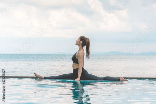 Asian young woman practice Yoga Monkey God Pose or Yoga Hanumanasana pose on the pool above the beach in the morning with beautiful sea in Tropical island,Feeling comfortable and relax in holiday