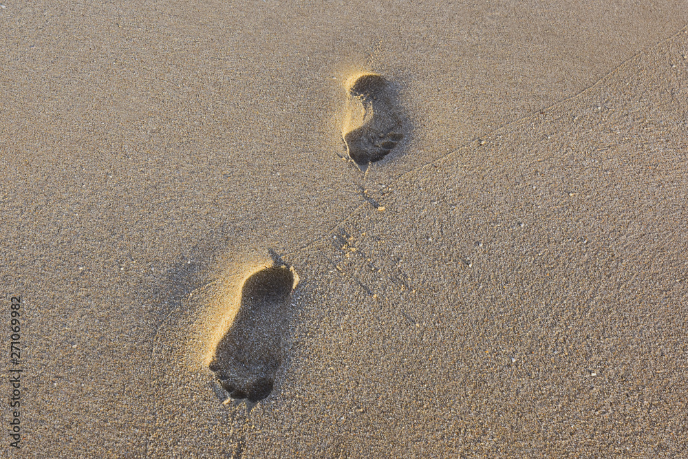 two human footprints in the fine sand at sunset