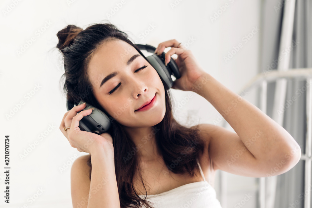 Beautiful young asia woman relaxing listening to music with  headphones on bed at home